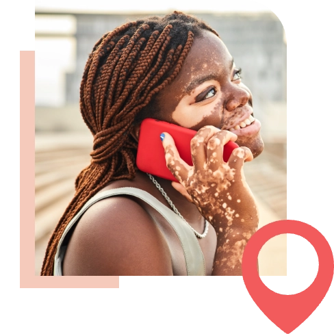 A young woman with vitiligo smiling and talking on her red cell phone up to her ear.